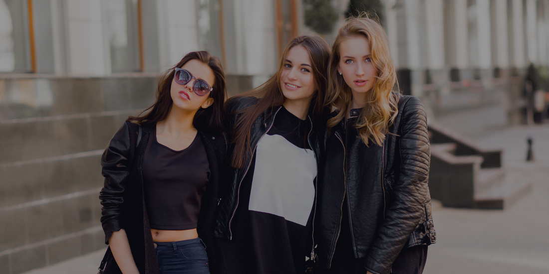 Three women posing together outdoors on a city street.


